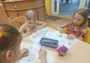 Dzieci siedzą przy stole i kolorują świetliki.