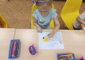 Dziecko siedzi przy stole i koloruje świetlika.