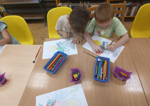 Dzieci siedzą przy stole i kolorują świetliki.