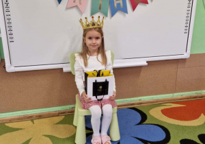 Jubilatka w koronie trzyma na kolanach torbę z cukierakami