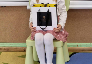 Jubilatka w koronie trzyma na kolanach torbę z cukierakami