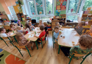 Dzieci siedzą przy stołach i jedzą poczęstunek