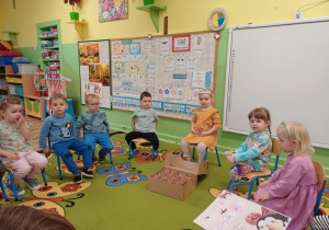 Dziewczynka siedzi na krześle wokół niej siedzą dzieci.