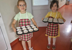 Dwie dziewczynki niosą blachy z muffinkami do kuchni
