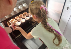 Dziewczynka wkłada blachę z muffinkami do piekarnika