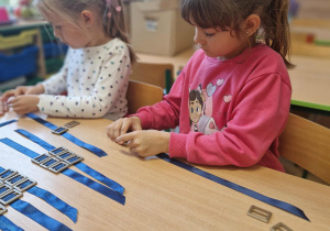 Dwie dziewczynki nawlekają guziki na tasiemkę