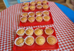 Na stole rozłożone są upieczone muffiny na czerwonych tacach