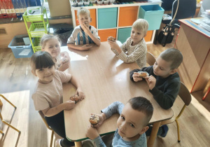 Dzieci siedzą przy stoliku i jedzą muffiny