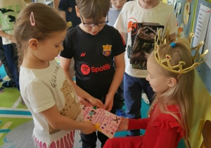 Dziewczynka i chłopiec wręczają jubilatce prezent -książeczkę z rysunkami od dzieci z grupy