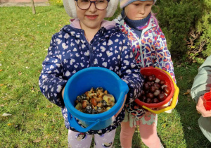 Dwie dziewczynki trzymają w ręku wiaderka z kasztanami i grzybami
