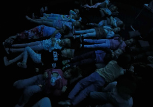 Dzieci leżą na poduszkach w namiocie i oglądają film edukacyjny