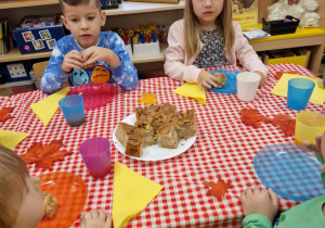 Dzieci siedzą przy stole i degustują owocowe ciasto