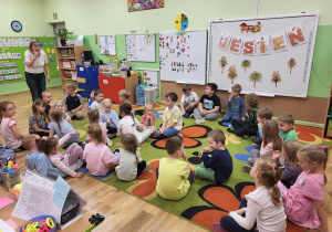 Dzieci siedzą na dywanie i słuchają Pani