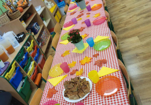 Stół przykryty obrusem w kratę zastawiony kolorowymi naczyniami