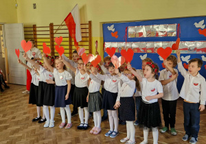 Dzieci z gr 4 machają czerwonymi serduszkami