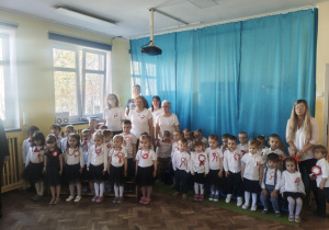 Dzieci oraz dorośli zgromadzeni w sali przygotowują się do odśpiewania hymnu