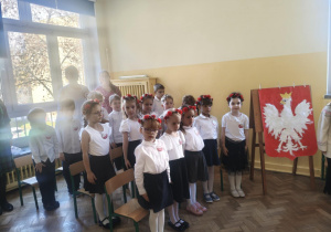 Dzieci oraz dorośli zgromadzeni w sali przygotowują się do odśpiewania hymnu