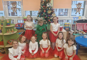 Dziewczynki w czerwonych spódnicach pozują na tle choinki