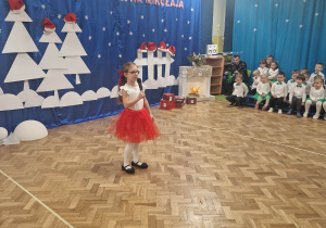 Dziewczynka w czerwonej spódnicy recytuje wiersz przez mikrofon