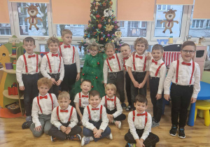 Chłopcy w czerwonych szelkach i muchach pozują do zdjęcia z choinką