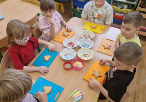 Dzieci dekorują ciasteczka kolorowymi posypkami