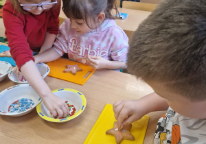 Dzieci dekorują ciasteczka kolorowymi posypkami