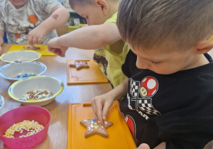 Dzieci dekorują ciasteczka kolorowymi posypkami