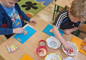 Dzieci dekorują ciasteczka kolorowymi posypkami