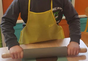 Chłopiec rozwałkowuje ciasto wałkiem