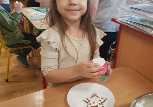 .Dziewczynka dekoruje piernik lukrem i posypką.