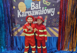 Chłopcy w przebraniach strażaków pozują na tle dekoracji