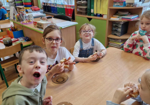 Dzieci siedzą przy stole i degustują pączki