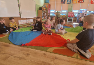 Dziewczynki siedza na kolorowej chuście czekaja na prezenty