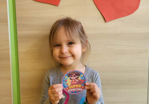 Dziewczynka stoi z medalem super dziewczynka
