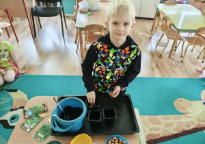 Chłopiec nasypuje ziemię do doniczki