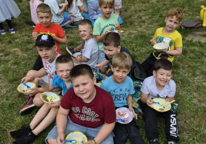 Chłopcy siedzą na macie piknikowej i jedzą desery lodowe