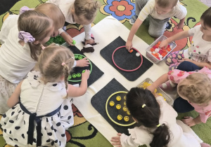 Dzieci uzupełniają kontur koła kolorowymi korkami