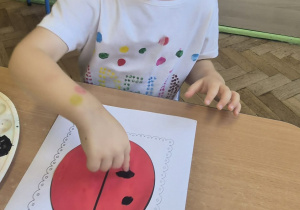 dziewczynka stempluje paluszkiem czarną kropkę na biedronce
