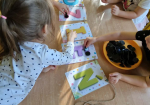 Dziewczynki układają czarne koła na literach napisu DZIEŃ KROPKI