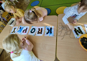 Dziewczynki układają czarne koła na literach napisu DZIEŃ KROPKI