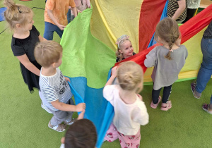 Dzieci zawijają jubilatkę w urodzinowy cukierek za pomocą chusty animacyjnej.