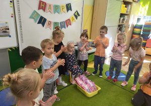 Dzieci śpiewają w kole sto lst jubilatce.