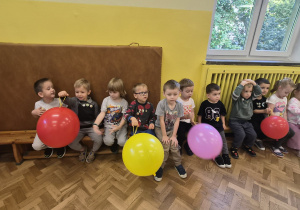 dzieci siedzą na łąweczce z balonami