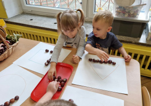 Dziewczynka i chłopiec układają kasztany na wzorze.
