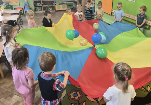 Dzieci uczestniczą w zabawie z chustą animacyjną i balonami