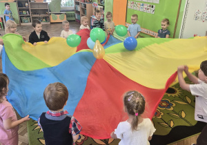 dzieci uczestniczą w zabawie z balonami i kolorową chustą
