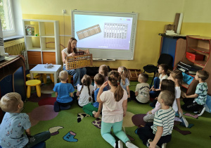 Dzieci siedzą i słuchają Pani prowadzącej zajęcia
