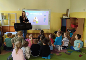 Dzieci siedzą i patrzą na tablicę multimedialną i Panią prowadzącą
