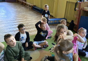 Dzieci siedzą na dywanie i zgłaszają się