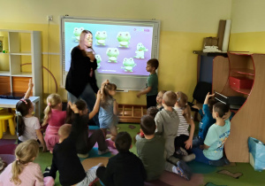 Dzieci siedzą i patrzą na tablicę multimedialną i Panią prowadzącą